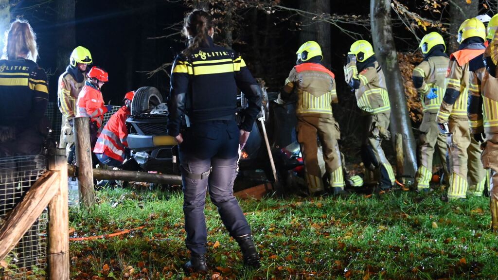 Auto ramt lantaarnpaal en bank en slaat over de kop, bestuurder bekneld